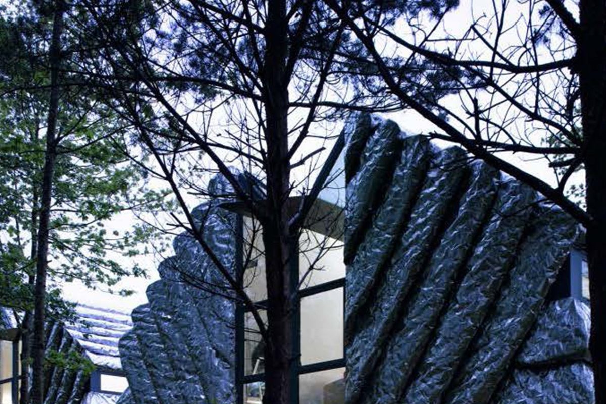 Small studio buildings with folded, crinkled metal roofs set among pine trees at dusk