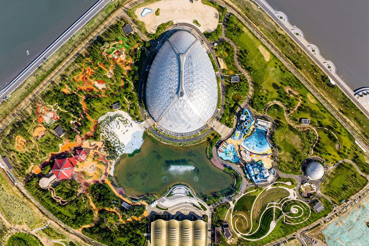 Aerial view of a domed visitor attraction set in landscaped gardens beside water